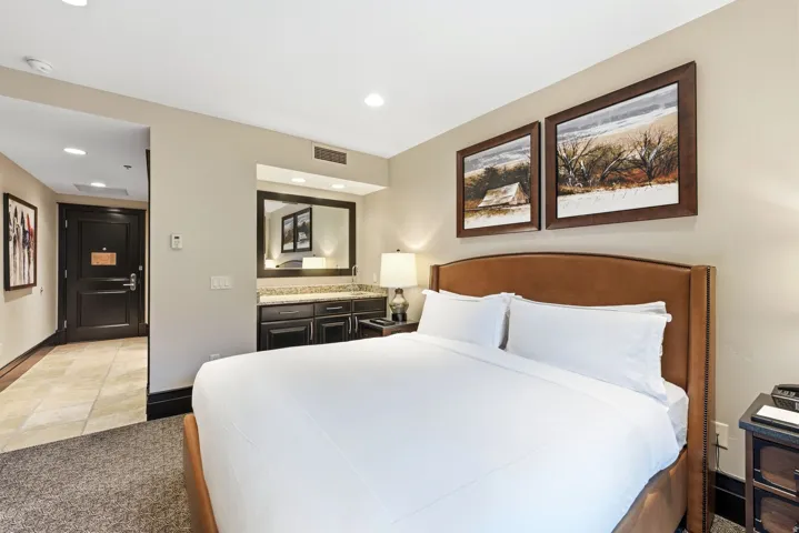 Spacious room featuring a large bed with a brown upholstered headboard, recessed lighting, and a dark wood door