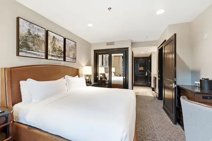 Spacious sleeping area featuring a padded headboard, recessed lighting, dark wood-finish doors, and a built-in desk with a stone-finish countertop