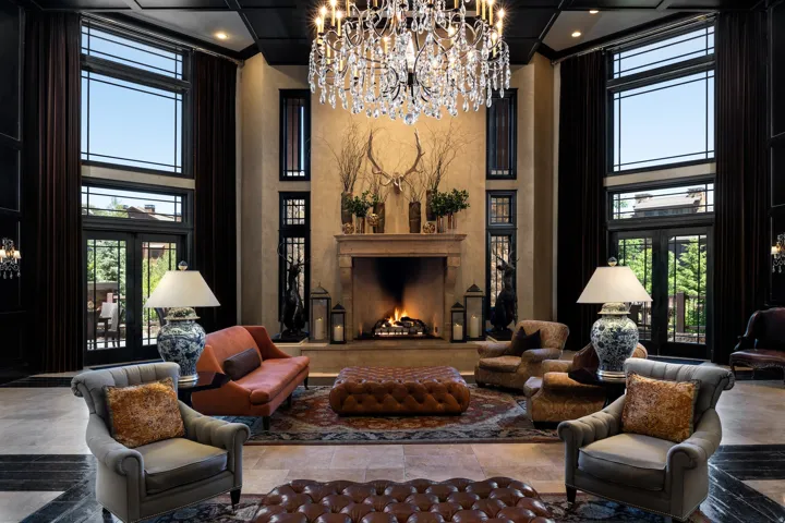Grand hall featuring a central fireplace with stone surround, a large crystal chandelier, and dark wood-paneled walls