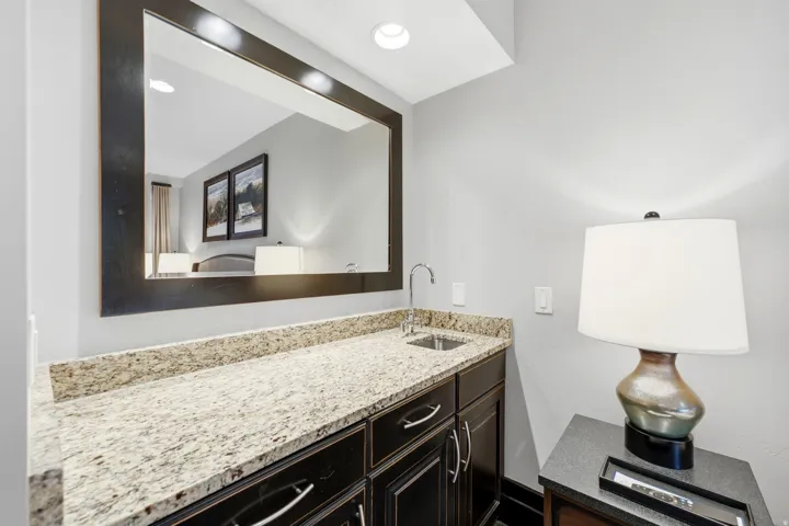 Built-in wet bar featuring a speckled countertop, undermount sink with gooseneck faucet, and dark wood cabinetry with chrome hardware