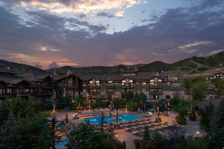 Large multi-story building featuring stone and wood siding, multiple balconies, and abundant exterior lighting