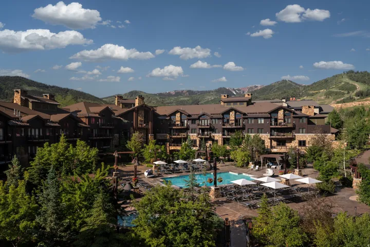 Expansive resort-style property featuring a large outdoor swimming pool, multiple lounging areas with umbrellas, and surrounding green landscaping
