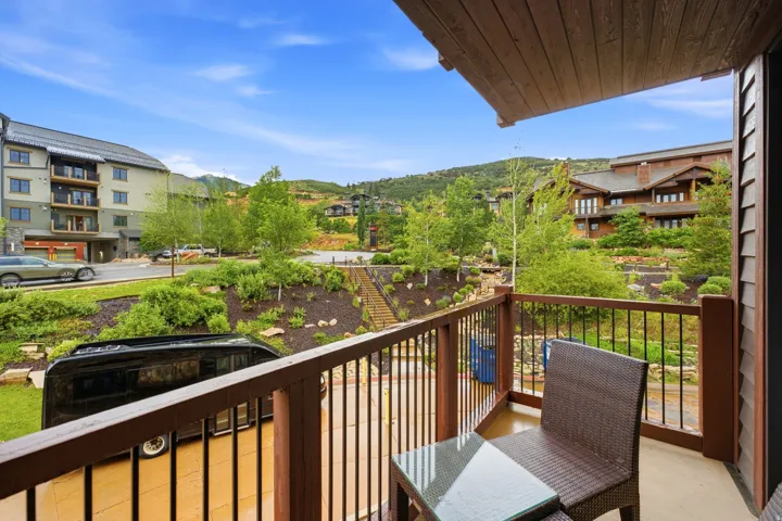 Private balcony featuring wood-finish railings with black balusters, overlooking a landscaped hillside with mature trees and a stepped pathway