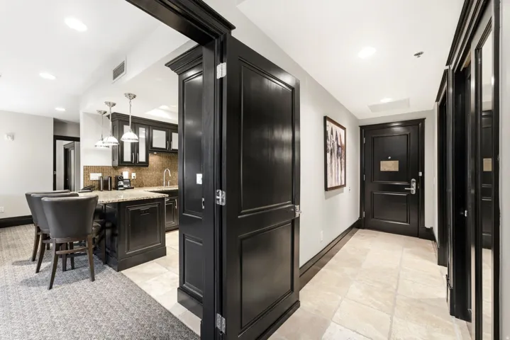 Entry foyer with light tile flooring leading to a built-in wet bar featuring dark cabinetry, stone countertops, and three pendant lights