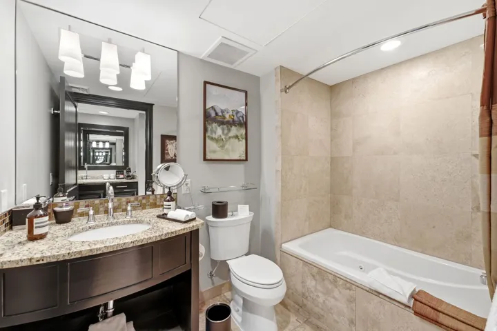 Bathroom featuring a deep soaking tub, single vanity with a granite countertop, undermount sink, and a mirrored wall
