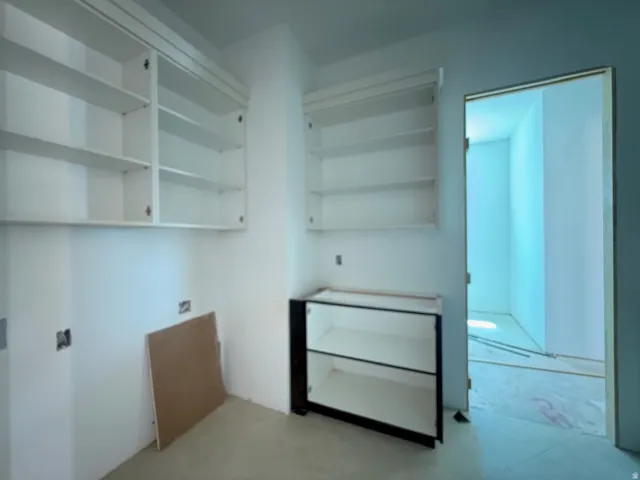 Modern kitchen featuring recessed shelving with glass-front cabinetry, stainless steel hardware, concrete flooring, and integrated appliances