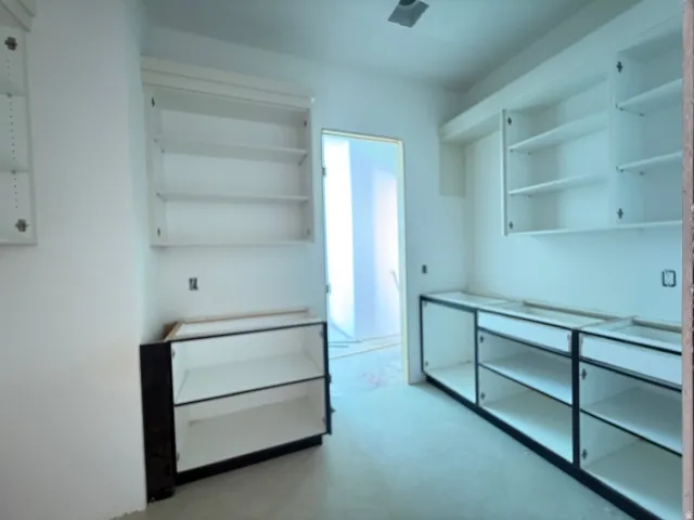 Modern walk-in closet featuring custom glass-front cabinetry with multiple storage drawers, white shelving units with glass doors, polished concrete flooring, and abundant natural light from an interior window