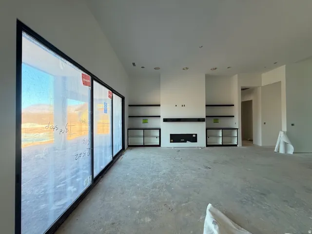 Open-concept living space featuring polished concrete flooring, recessed ceiling lighting, and a custom built-in entertainment wall with integrated shelving and a linear fireplace insert