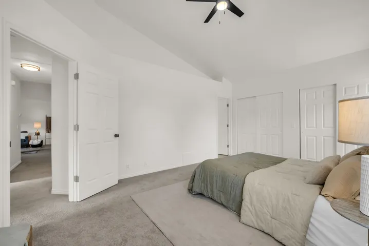 Spacious bedroom featuring vaulted ceilings, plush carpet flooring, two paneled doors, two sliding closet doors, and a ceiling fan with integrated lighting