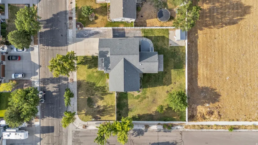 Aerial perspective of a single-family residence featuring a dark gray shingle roof, a concrete driveway, and a partially fenced backyard with established trees