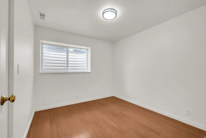 Room featuring wood-finish flooring, white baseboards, and a window with a well-style enclosure