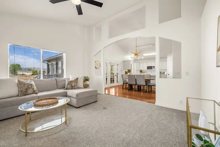 Bright living area featuring vaulted ceilings, a ceiling fan, and large windows with horizontal blinds