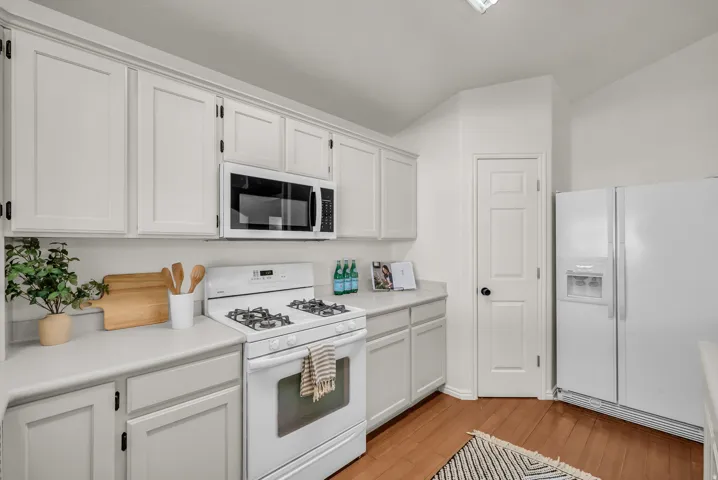 Kitchen featuring white cabinetry, light-toned countertops, wood-finish flooring, a white gas range, and a built-in microwave