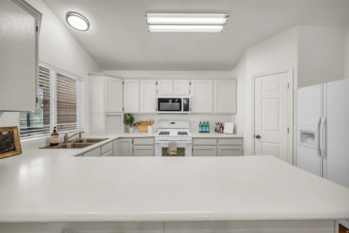 U-shaped kitchen featuring light-colored countertops, white cabinetry, and a double basin sink