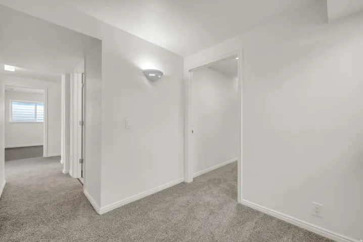 Hallway featuring light gray carpet flooring, white walls, white trim, and a wall-mounted sconce