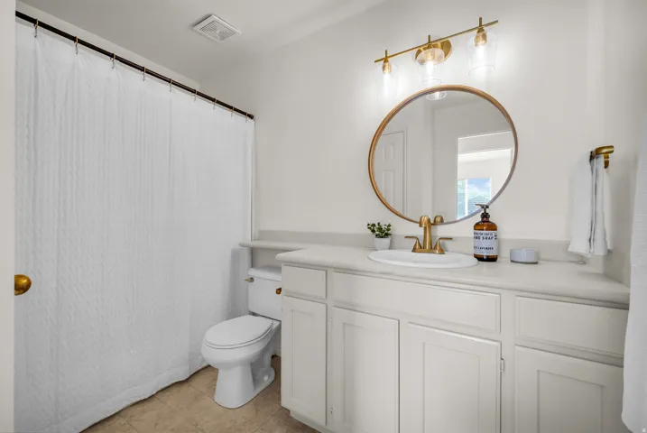 Bathroom featuring a white vanity with built-in storage, a drop-in sink, and a single-handle faucet with a brushed gold finish