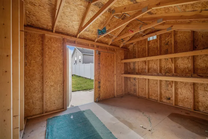 Spacious utility shed featuring exposed wood framing, a durable wood-finish floor, and integrated wall shelving