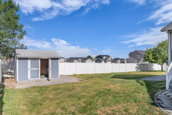 Expansive backyard featuring a lush lawn, a detached storage shed with a shingled roof, a concrete pad, a full privacy fence, and mature trees