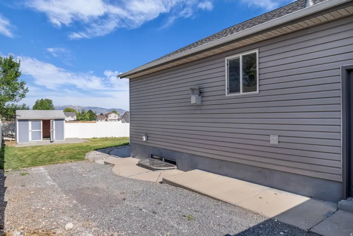 Light gray horizontal siding with a white-trimmed window, a concrete path, and a gravel surface