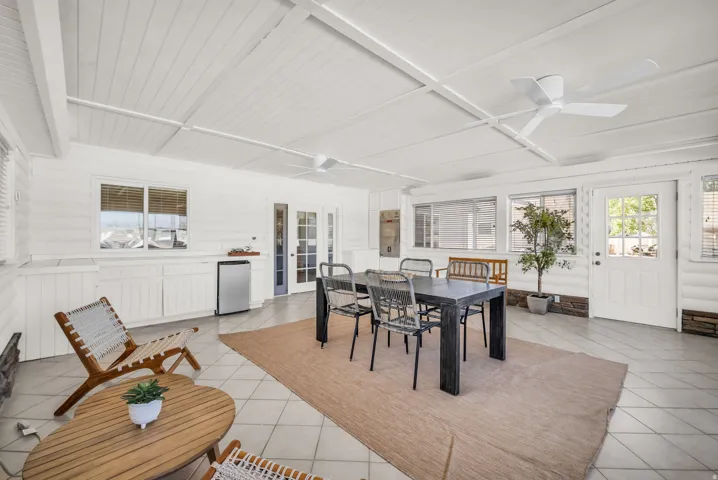 Covered patio featuring a white tongue-and-groove ceiling, tile flooring, multiple windows with horizontal blinds, and a built-in cabinet with integrated mini-fridge