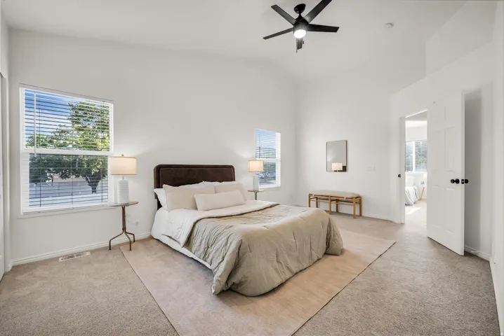 Spacious bedroom featuring vaulted ceilings, a ceiling fan, two windows with blinds, and neutral carpet flooring