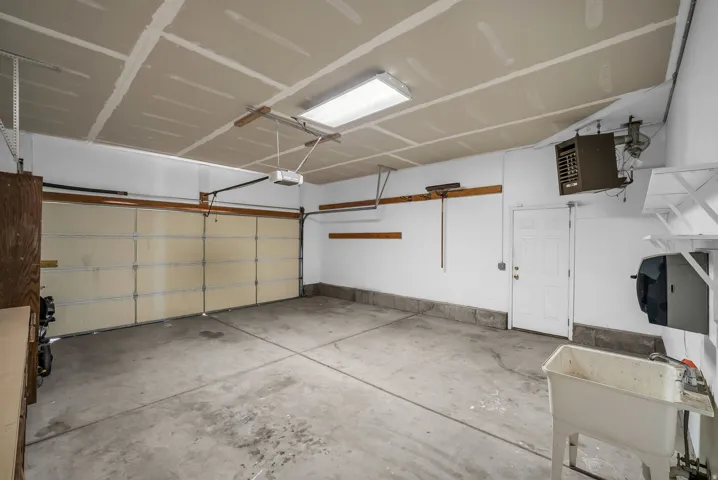 Spacious garage featuring a sectional garage door, concrete flooring, utility sink with a faucet, built-in shelving, and a wall-mounted heater