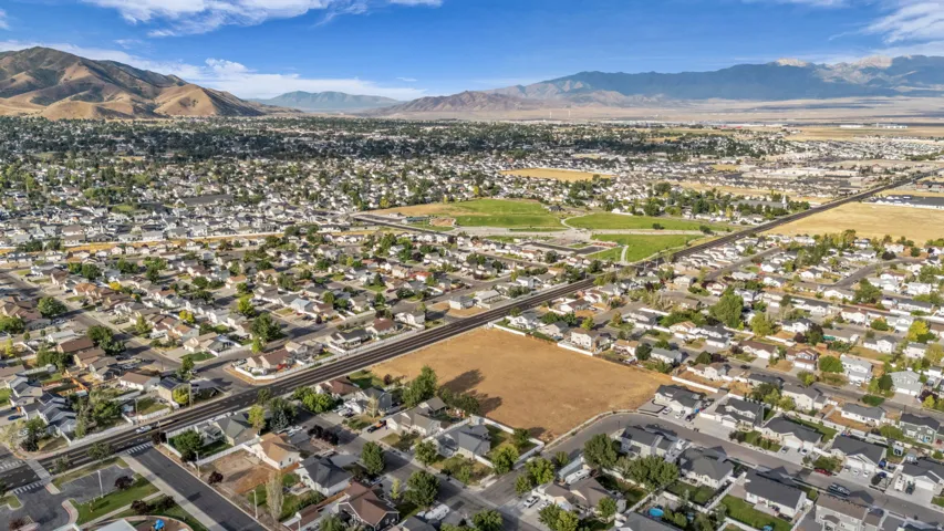 Expansive residential area featuring a distinct mountain backdrop, a prominent open field, and numerous single-family homes