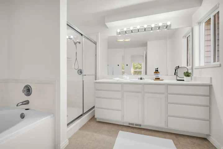 Bathroom featuring a spacious vanity with extensive storage, a large wall-mounted mirror, and an adjacent window for natural illumination