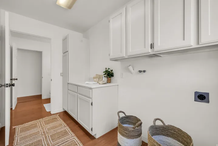 Dedicated laundry space featuring wood-finish flooring, white cabinetry, and a light-toned countertop