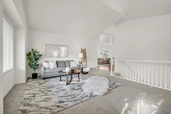 Spacious living area featuring neutral carpeting, white walls, and a vaulted ceiling