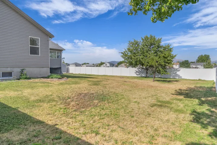 Spacious rear yard featuring a large lawn area, mature trees, and a full-height vinyl privacy fence