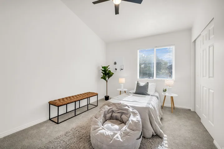 Carpeted room featuring a single window with blinds, a ceiling fan, and a white paneled bi-fold closet door