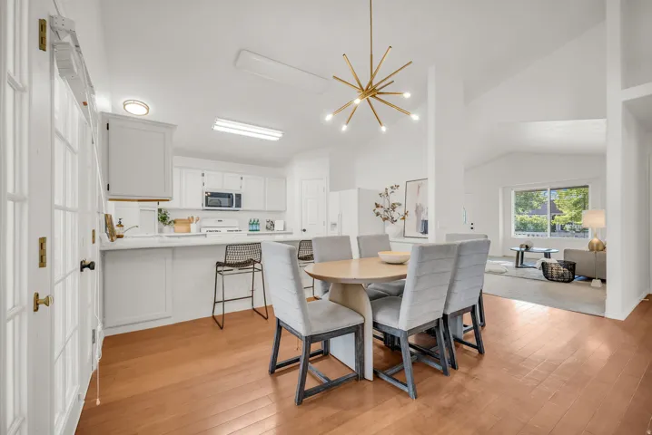 Open-concept dining area featuring wood-finish flooring, a contemporary chandelier, vaulted ceilings, and a breakfast bar with white cabinetry