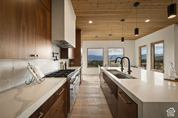 Modern kitchen featuring extensive wood-finish cabinetry, white countertops, a professional-grade range, and a large island with an integrated sink and dual faucets