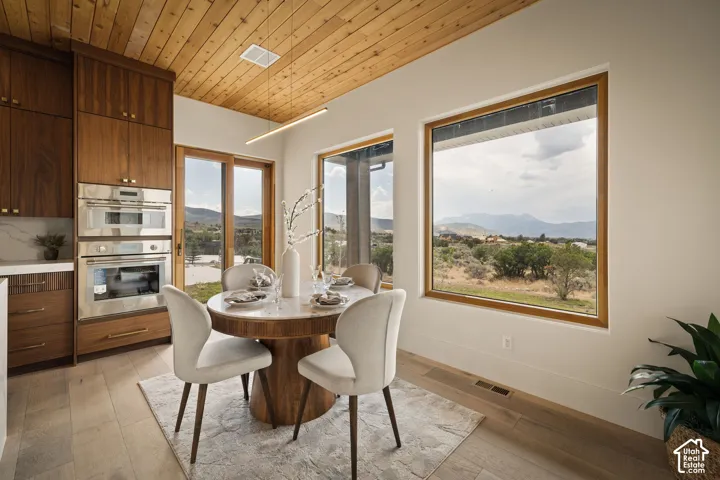 Dining area with large windows, a wood-plank ceiling, built-in stainless steel double ovens, and rich wood cabinetry