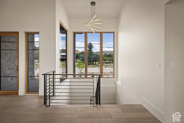 Architectural staircase featuring a linear chandelier, wood-finish flooring, and modern iron railings
