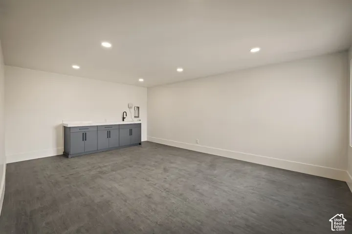 Spacious room featuring dark wood-finish flooring, recessed lighting, and a built-in wet bar with gray cabinetry, a light-toned countertop, and a black faucet