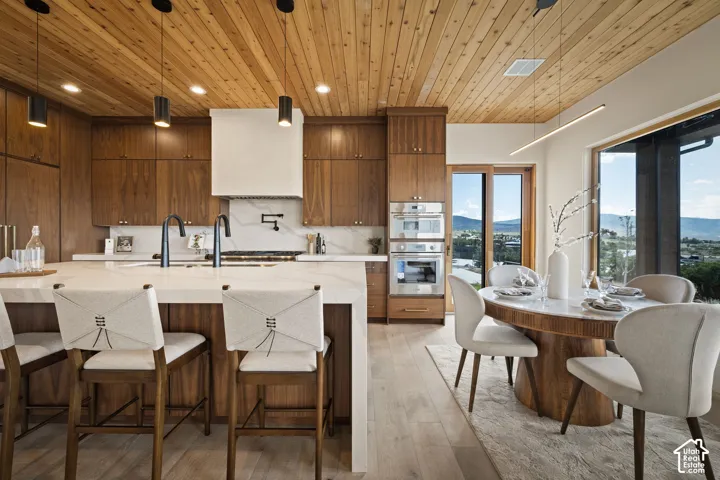 Gourmet kitchen featuring a wood-plank ceiling, integrated wood cabinetry, a large center island with a stone countertop, built-in double ovens, and a dining area with expansive windows