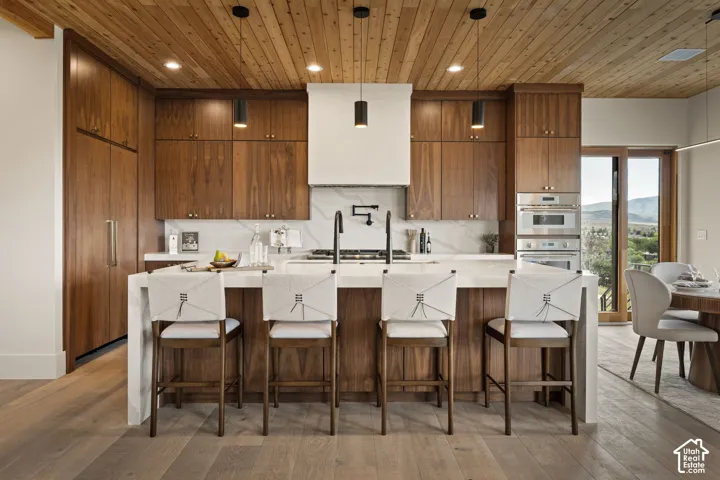 Kitchen featuring custom wood cabinetry, a large center island with seating, integrated appliances, built-in wall oven and microwave, and wood-paneled ceilings