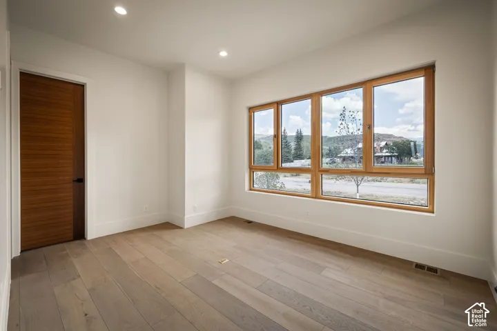 Bright interior space featuring wood-finish flooring, a contemporary wood door with a matte black handle, and recessed ceiling lighting