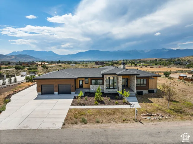 Modern ranch-style residence featuring a prominent stone facade, wood paneling, and a dark shingle roof