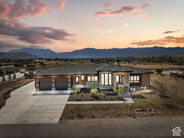Modern architectural design featuring extensive window placements, a multi-car concrete driveway, a two-car garage, and a stone and wood-paneled exterior