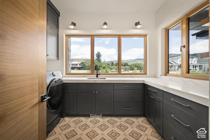 Laundry room featuring extensive counter space with a built-in sink, ample cabinetry, wood-finish window frames, and decorative tiled flooring