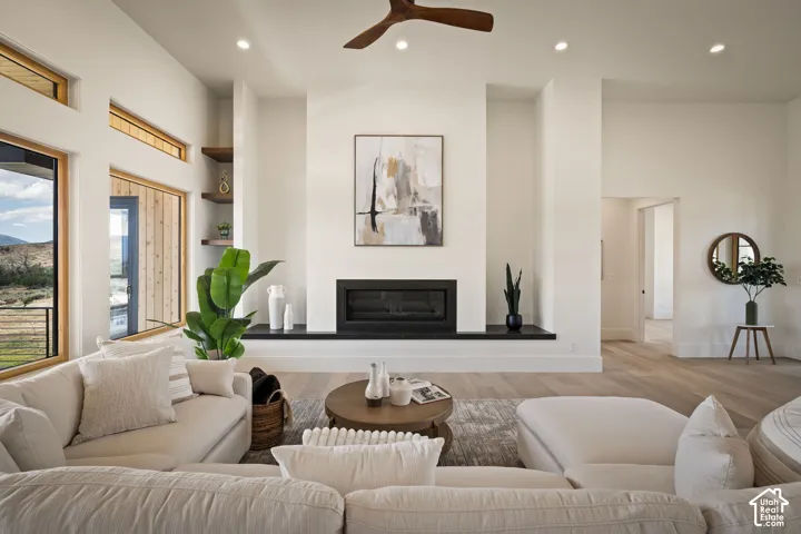 Spacious living area featuring high ceilings, a contemporary fireplace with a dark mantel, wood-finish flooring, and recessed lighting