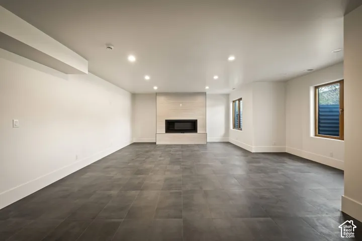 Spacious room featuring dark tile flooring, a modern fireplace with light-toned stone surround, recessed lighting, and multiple windows