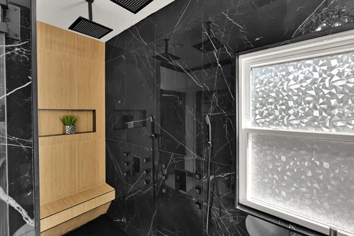 Shower with black marble-style tiling, integrated bench seating, and an in-wall niche
