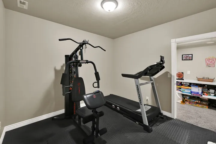 Dedicated exercise room featuring dark rubber flooring, light neutral-toned walls, and a ceiling-mounted light fixture