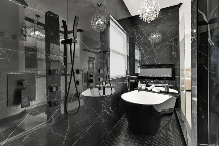 Luxurious bathroom featuring floor-to-ceiling black marble-patterned walls, a standalone black bathtub, and a modern wall-mounted fireplace