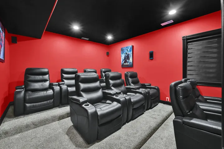 Dedicated home theater featuring tiered seating, recessed ceiling lighting, wall-mounted speakers, and a large window with privacy blinds