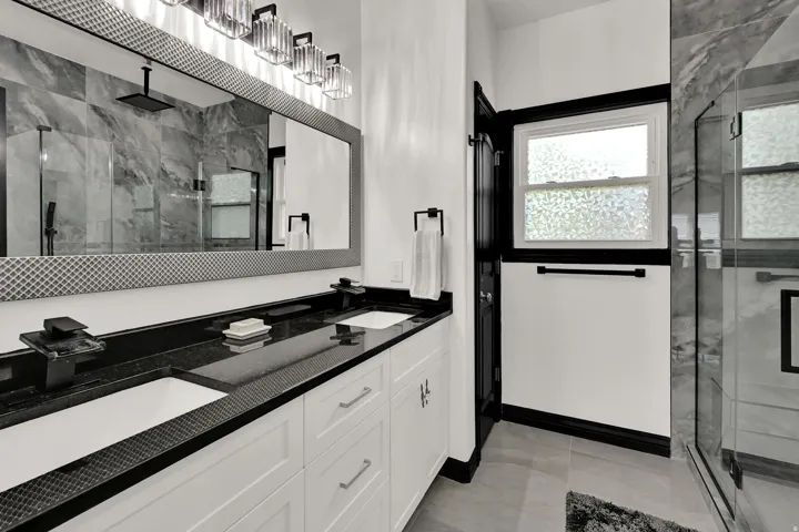 Dual vanity with black countertops, white shaker cabinetry, and black hardware
